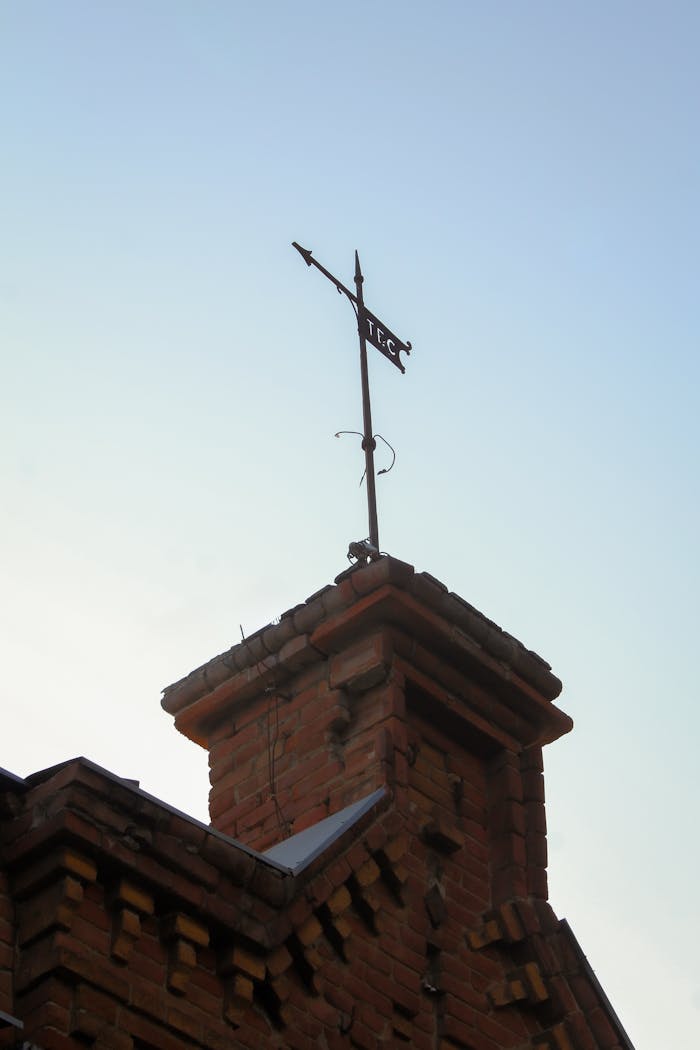 A historic brick chimney topped by a weather vane against the clear sky in Tbilisi, Georgia.