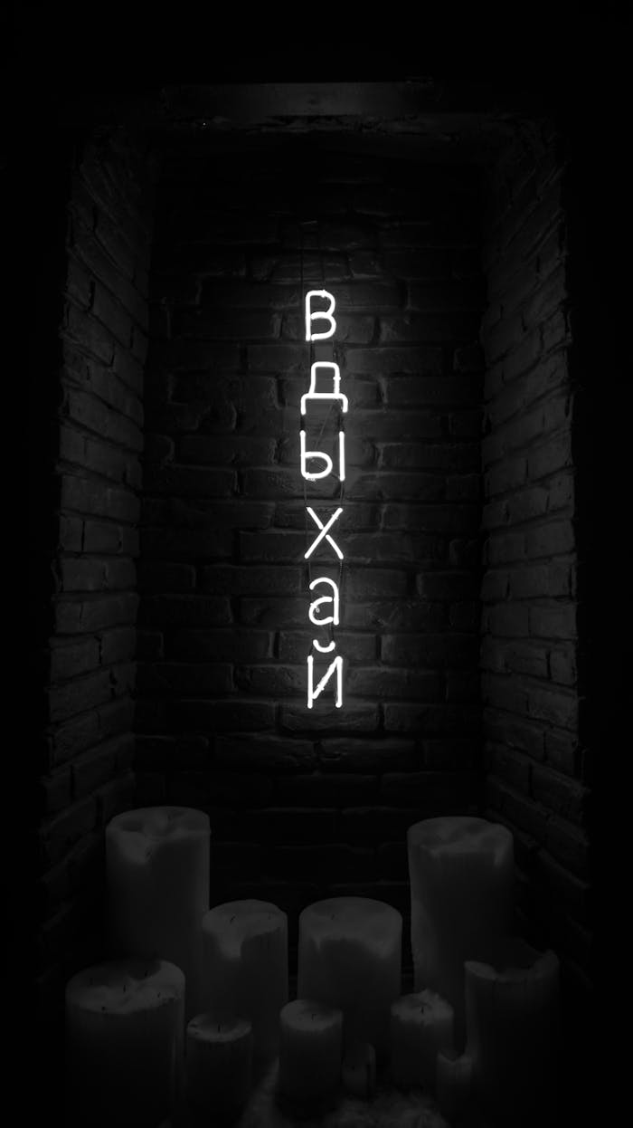Vertical black and white image of a neon sign in Cyrillic with candles below.
